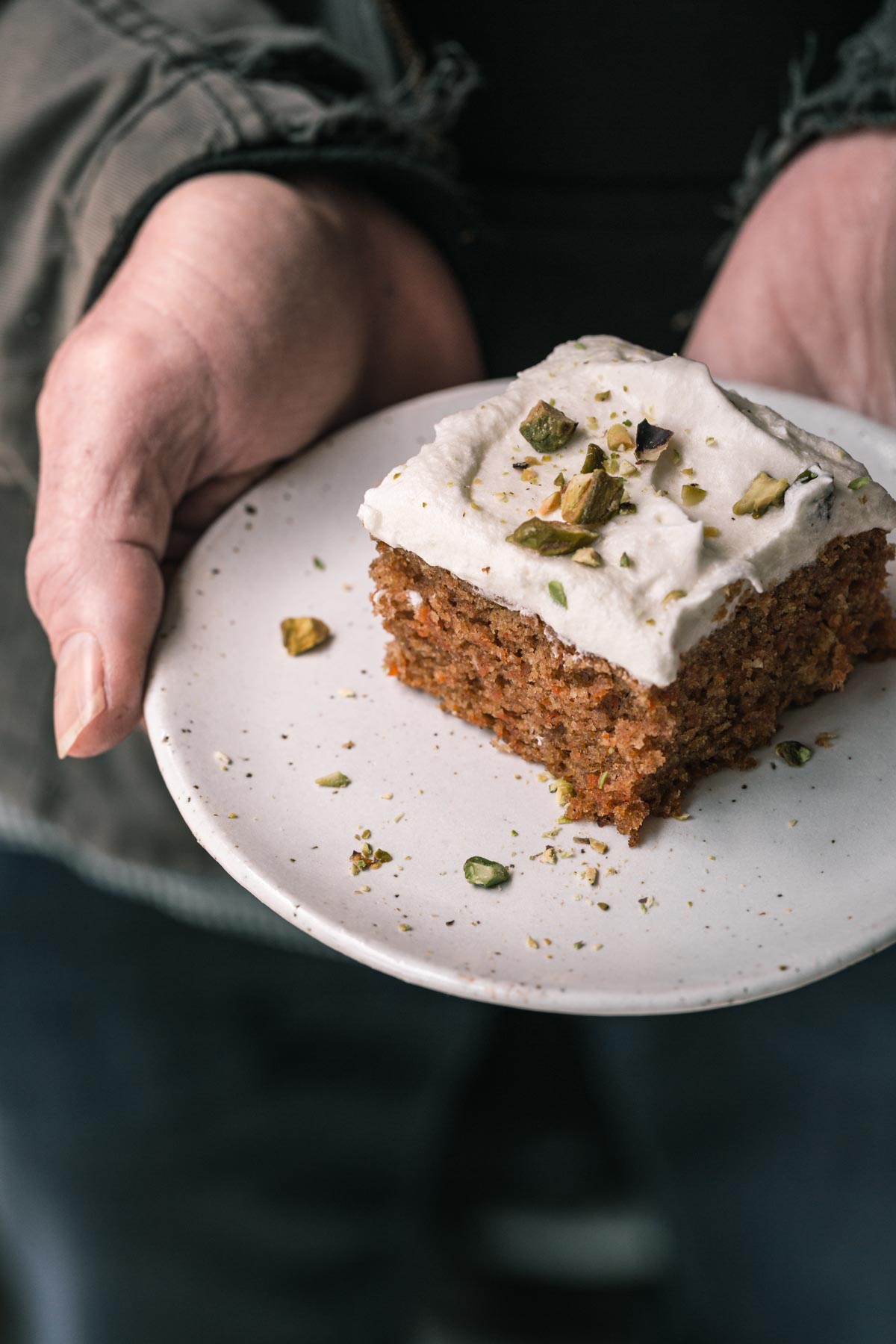Hands holding a square of carrot cake.