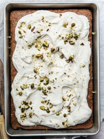 A slab of carrot cake with frosting and nuts.