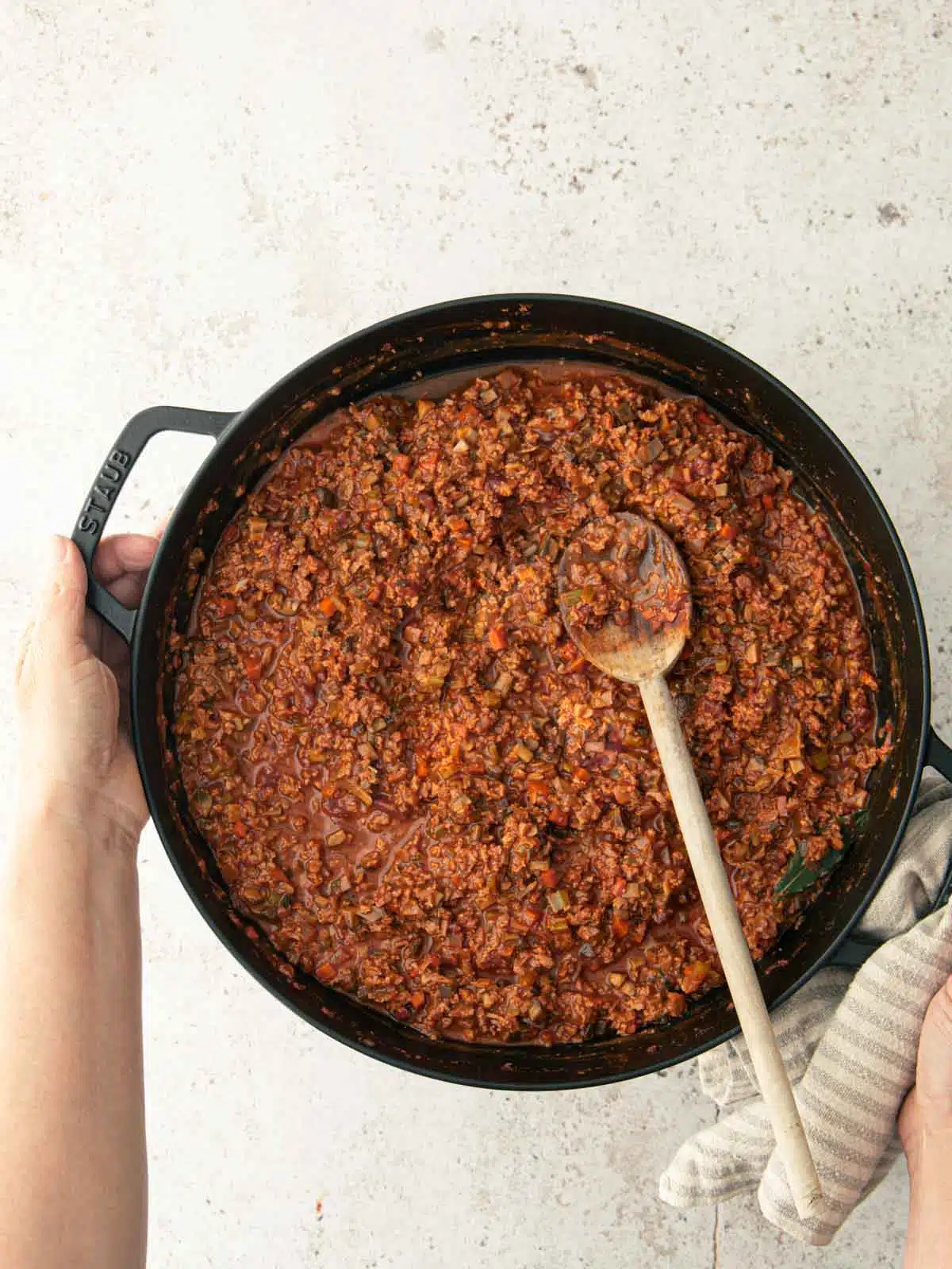 A woman's hands holding a large pan of bolognese sauce. 