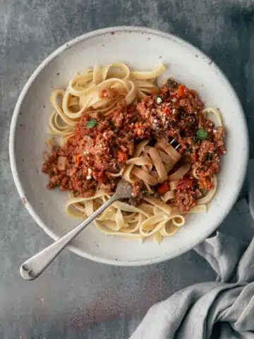 A bowl off pasta bolognese with a napkin.