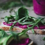Beetroot hummus on bread with greens on a wooden board.