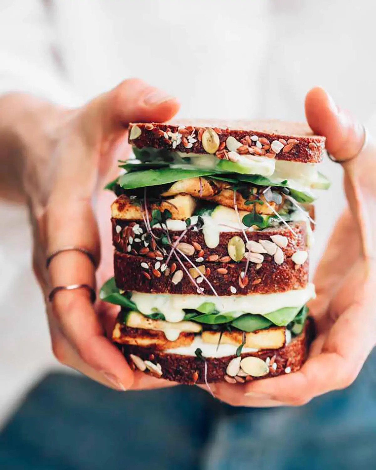 A woman holding a stacked cheese and vegetable sandwich.