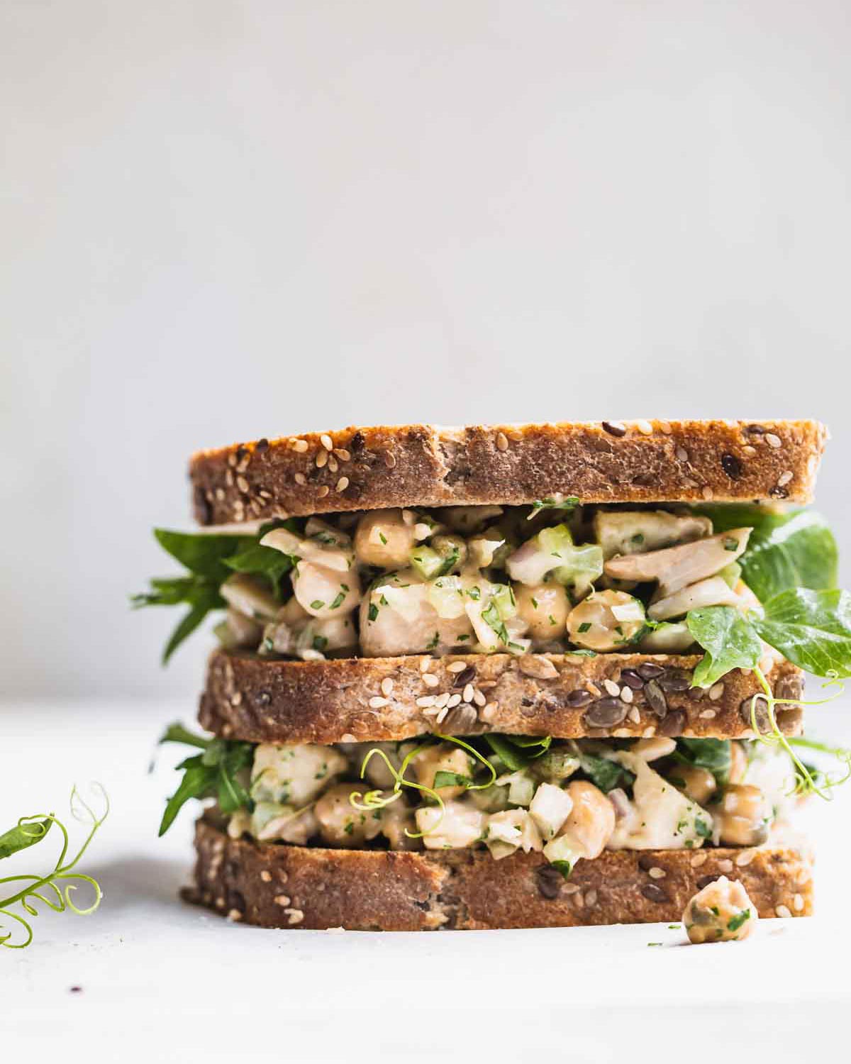 A stacked sandwich with greens on a white background.
