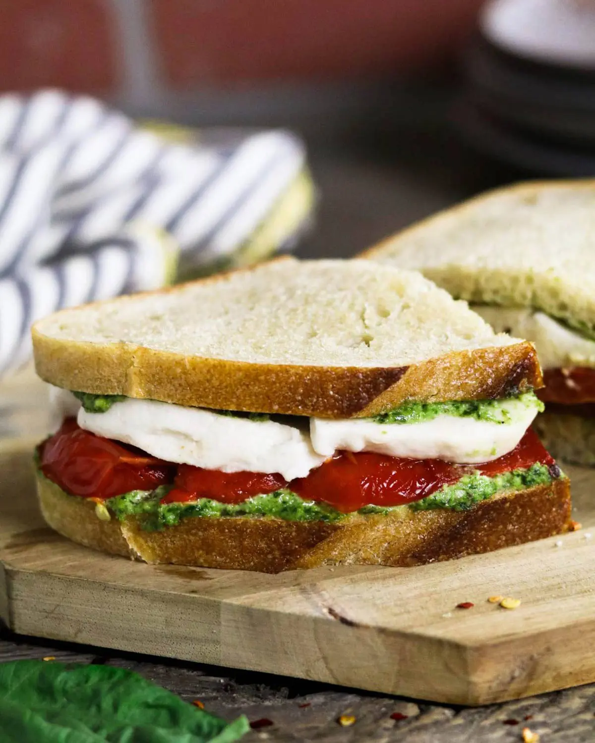 A pesto, tomato and cheese sandwich on a board.