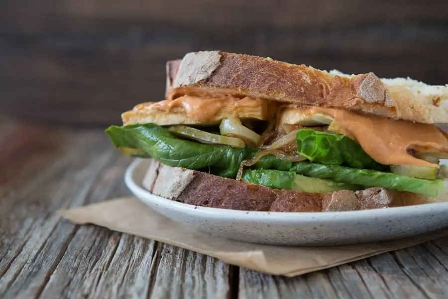 Toasted tofu sandwich with greens on a plate. 