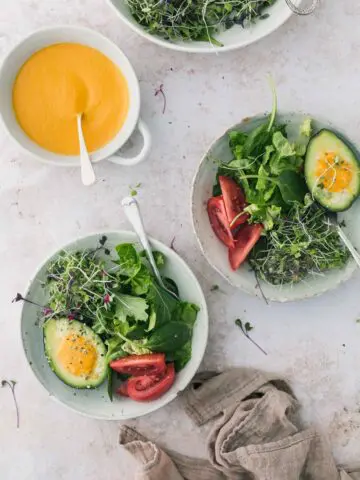 Bowl of green salad with a bowl of carrot salad dressing.