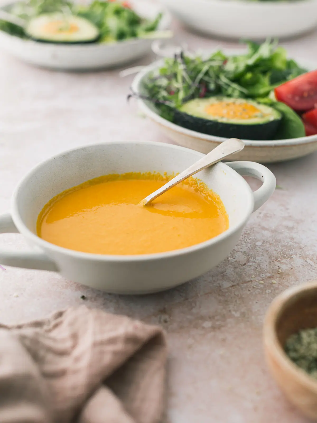 A bowl of carrot ginger salad dressing on a table of salads.