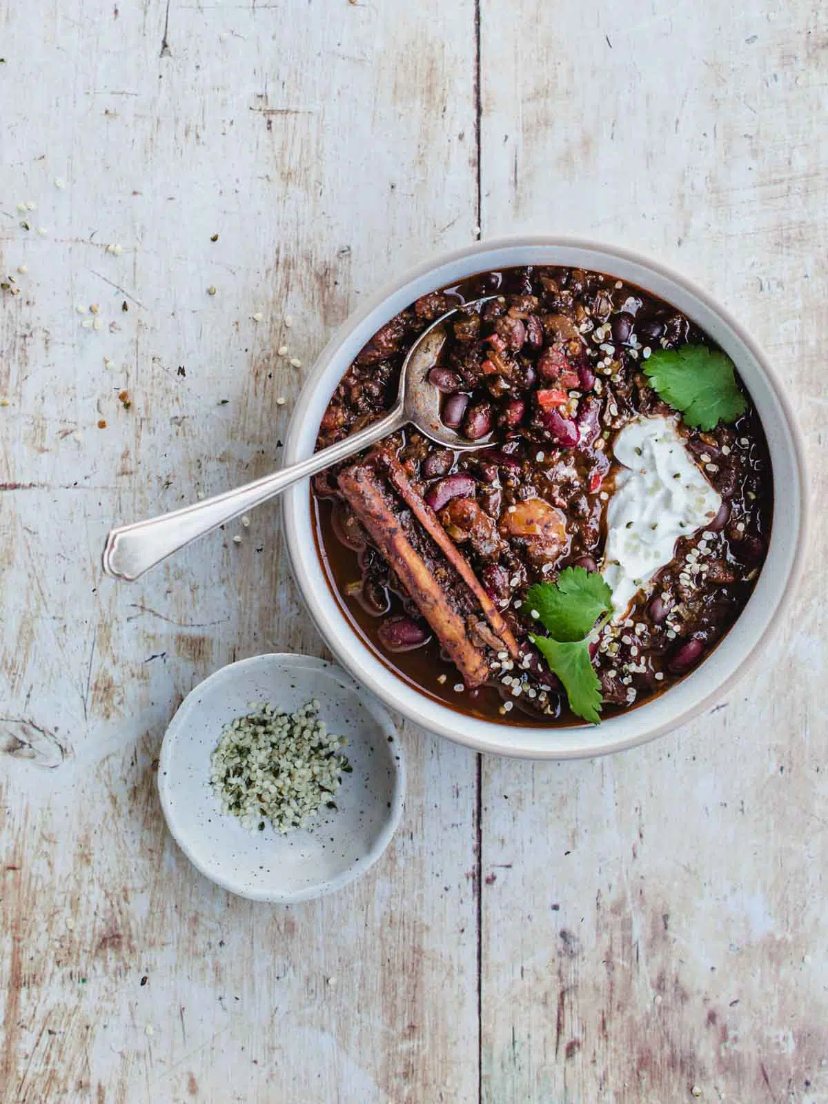 A bowl of chilli and a bowl of hemp seeds on a wooden background.