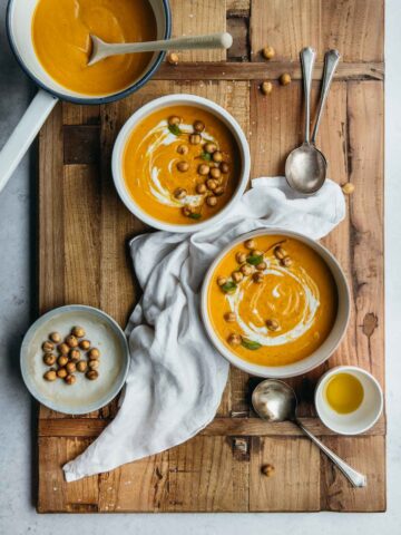 Bowls of pumpkin soup on a wooden board with chickpeas.