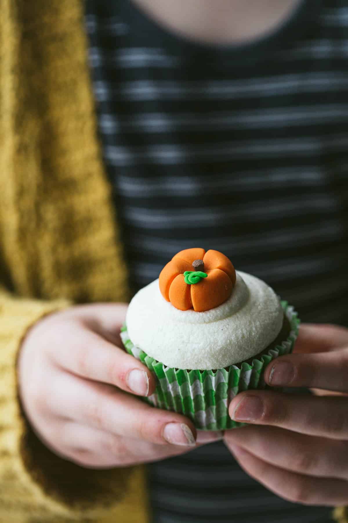 Little girl holding a cupcakes with a pumpkin topper.