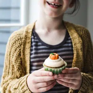 A little girl holding a pumpkin cupcake.