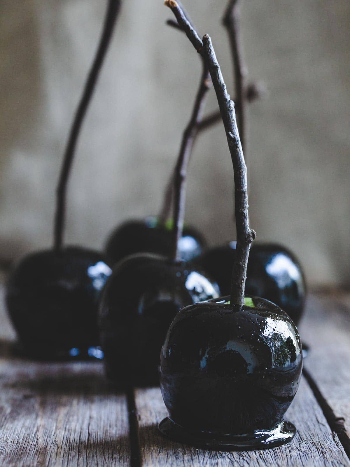 Shiny black toffee apples with sticks on a wooden table. 