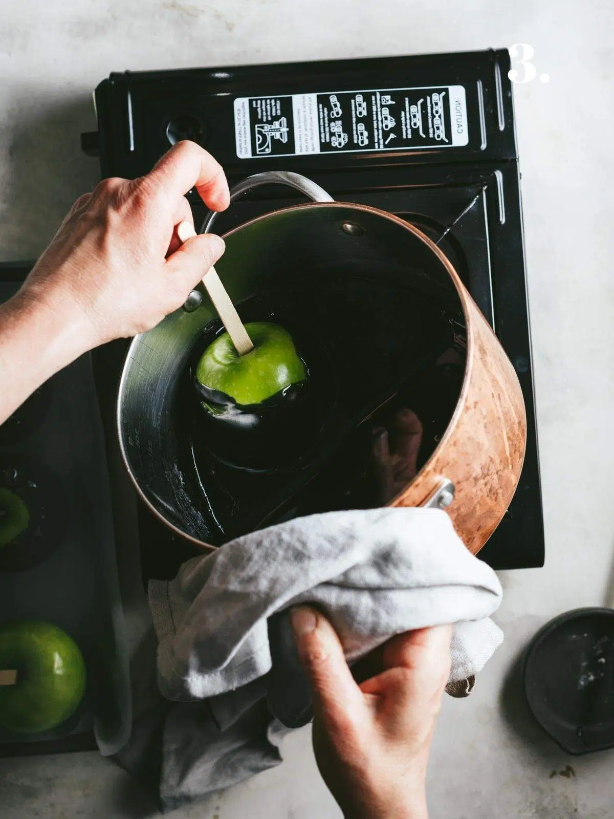 An apple being dipped in black toffee.