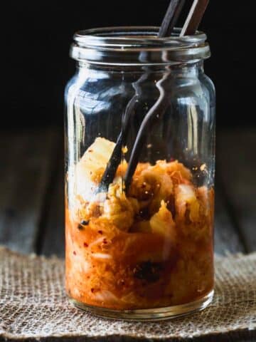 A glass jar half filled with kimchi and wooden chopsticks.