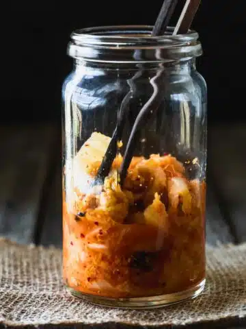 A glass jar half filled with kimchi and wooden chopsticks.