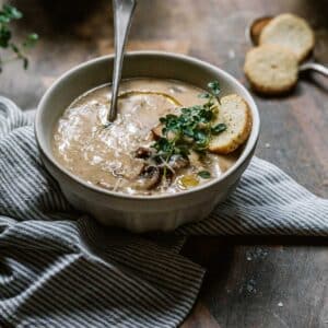 A bowl of vegan mushroom soup with thyme and croutons.