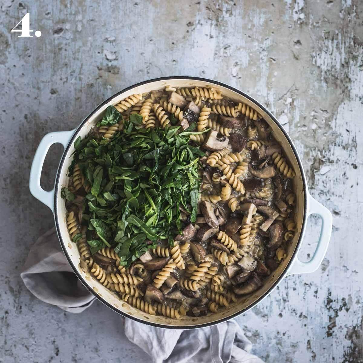 Cooked mushrooms pasta with chopped spinach in a large pot. 