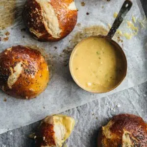 Pretzel buns with mustard sauce on paper.