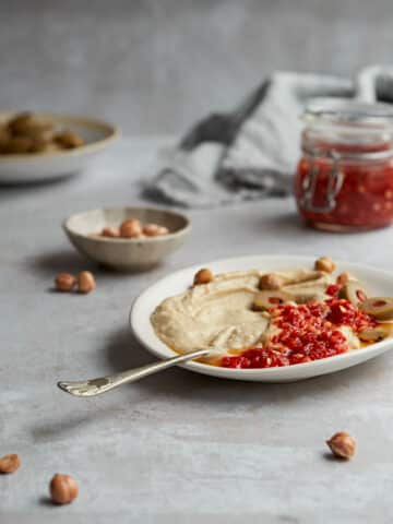 A table setting with a plate of hummus and chilli paste.
