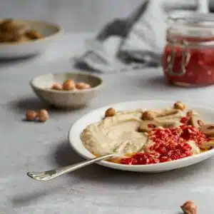 Hummus and chilli sauce own a plate with olives.