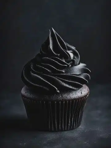A black cupcake with black frosting on a dark background.