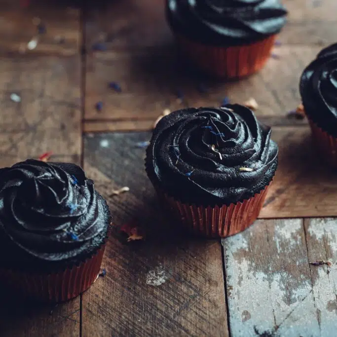 Black cupcakes on a rustic wooden table.