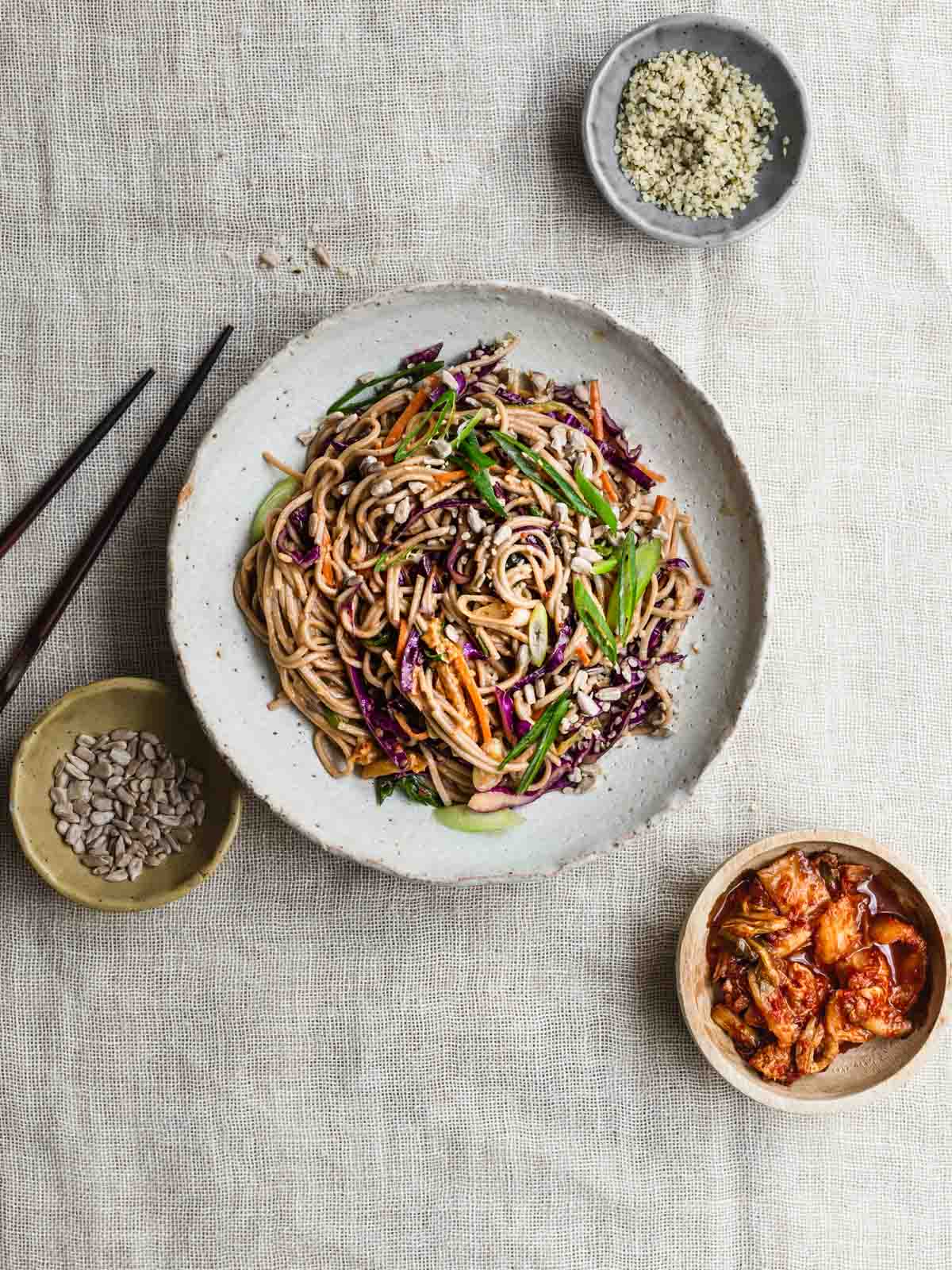 A bowl of noodle salad with kimchi and seeds.