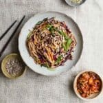 A bowl of kimchi noodles with condiments.