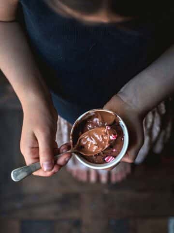 Little girl holding a pot of chocolate mousse.