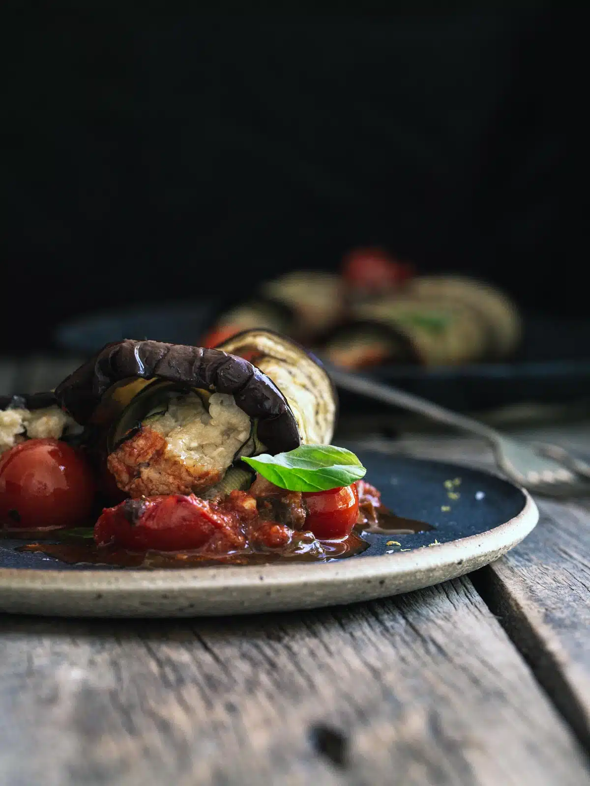 An stuffed eggplant roll with tomatoes on a plate.