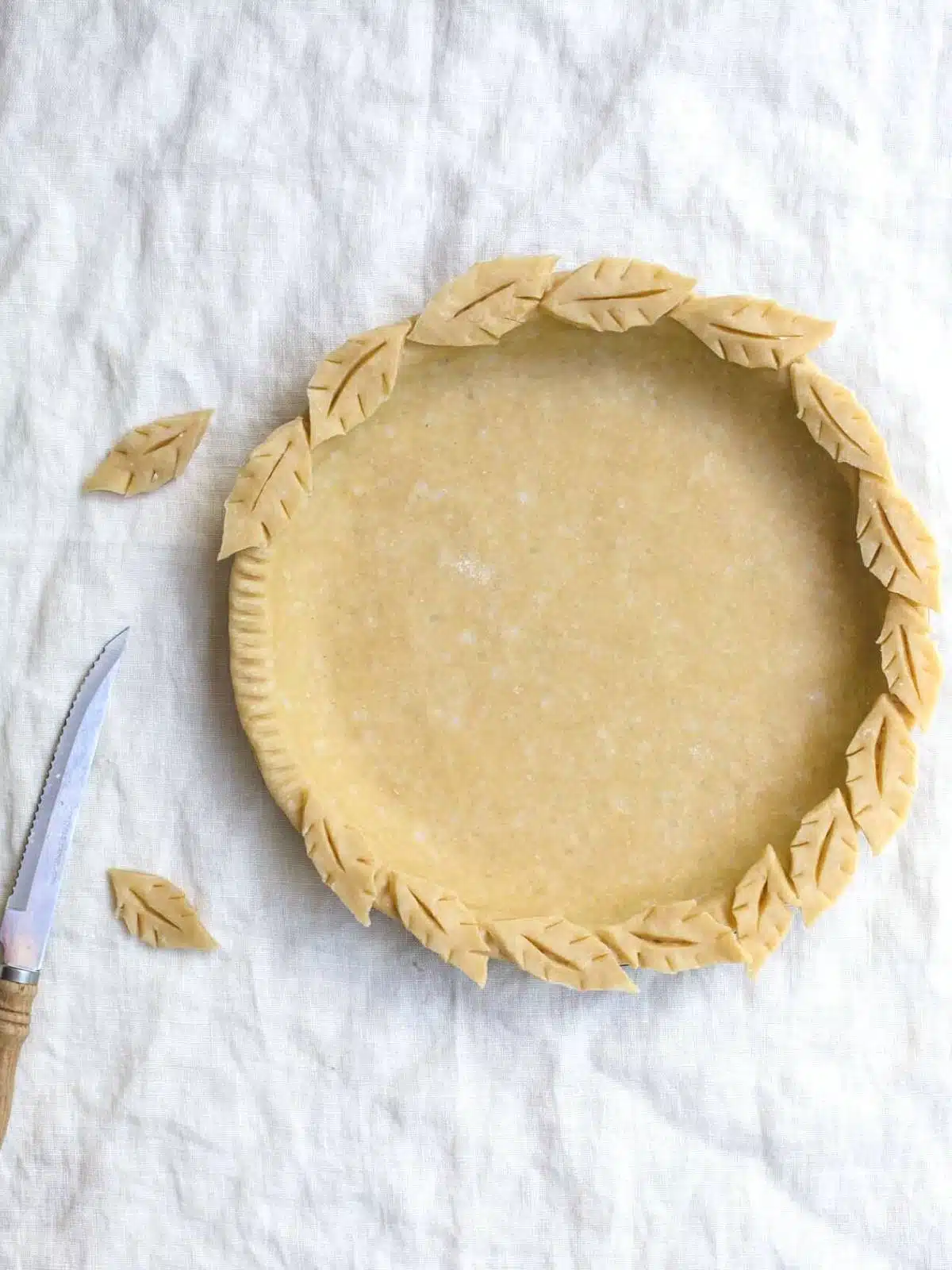 Finished pie crust pastry in a pie tin with pastry leaves.