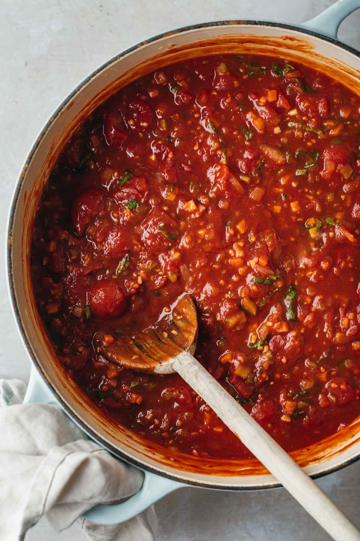 A large pot of homemade tomato sauce with a wooden spoon.