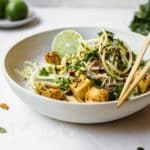 A bowl of noodle and tofu salad on a bench.