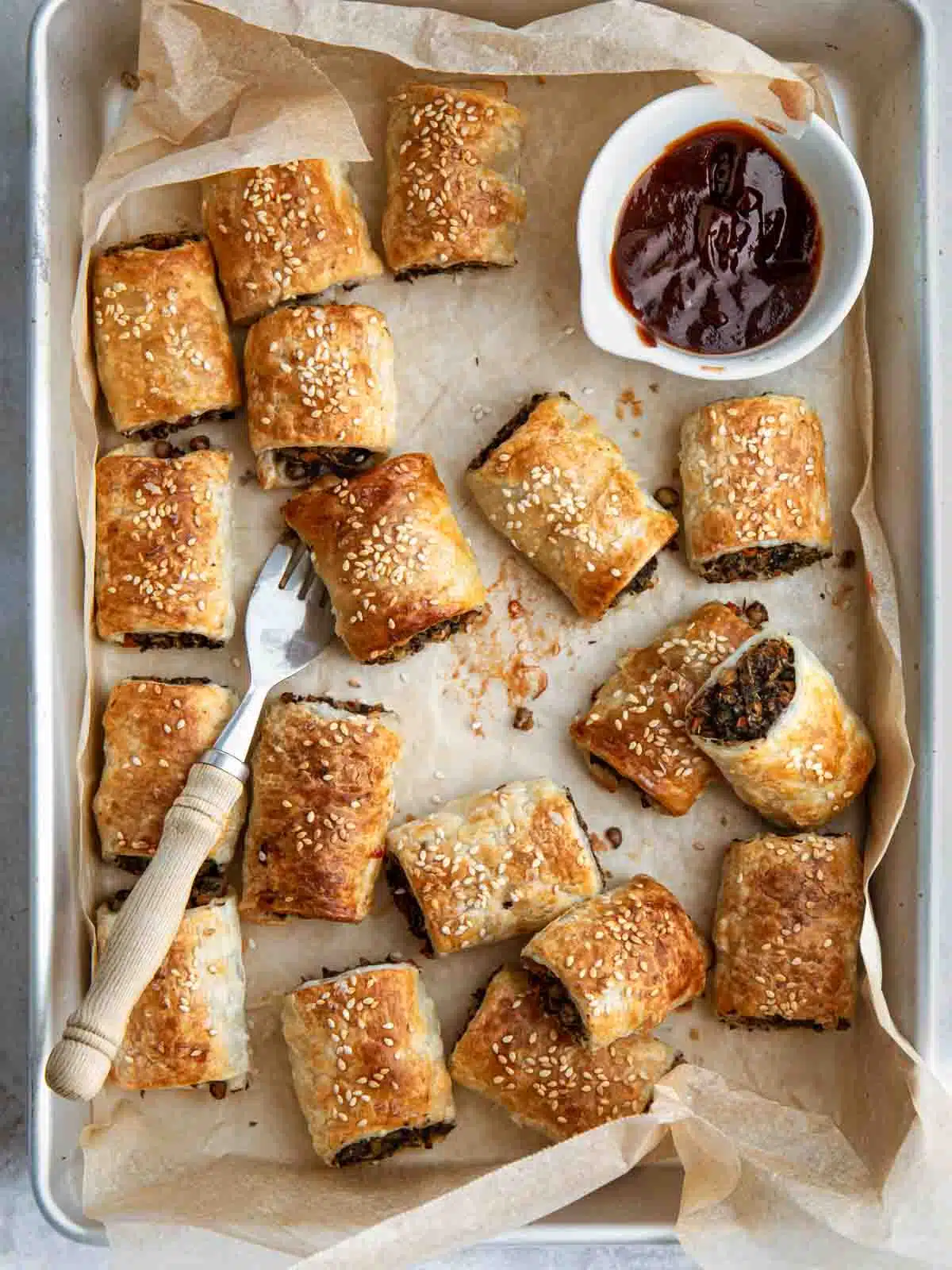A tray of sausage rolls with sauce.