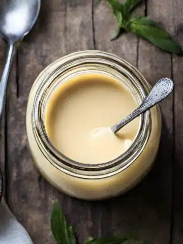 A jar of sauce with a spoon on a table.