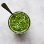 An overhead image of a jar of green kale pesto with a spoon