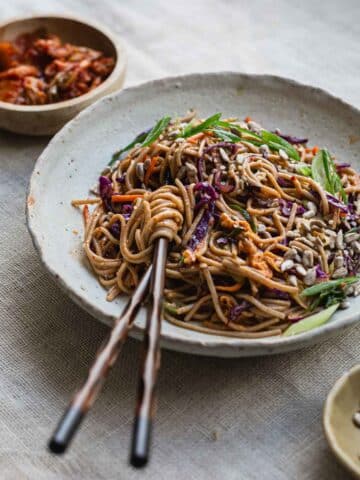 A bowl of kimchi noodle salad on a table cloth.