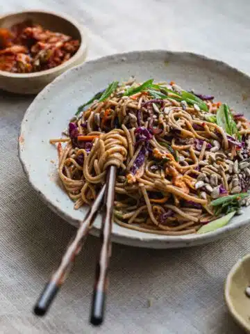 A bowl of kimchi noodle salad on a table cloth.