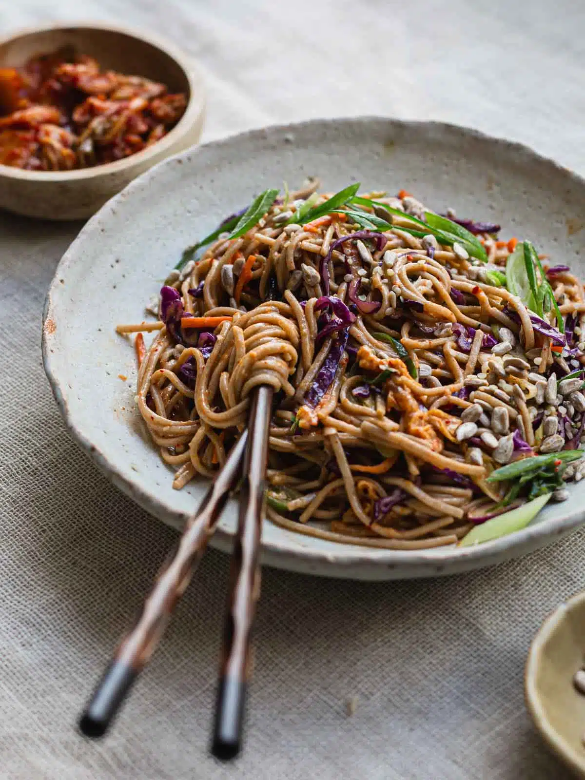 A bowl of kimchi noodle salad on a table cloth.