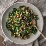 A bowl of kale and quinoa salad with lentils, currents and nuts in a bowl with a spoon.