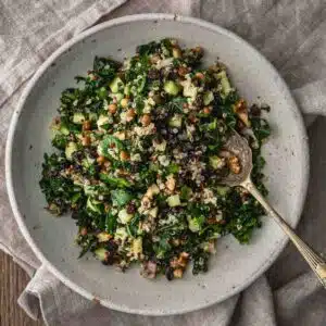 A bowl of kale and quinoa salad with lentils, currents and nuts in a bowl with a spoon.