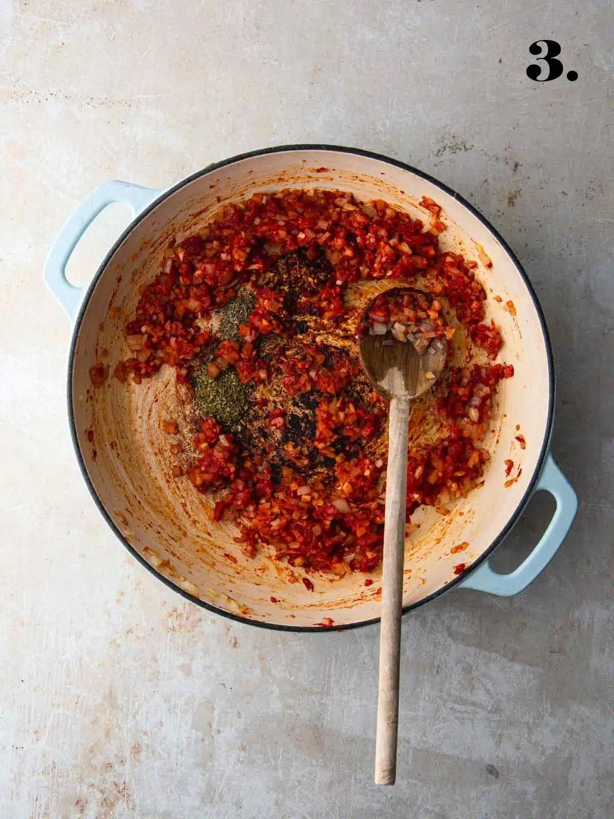 Onions and sun-dried tomatoes sautéing in a large pan with spices.