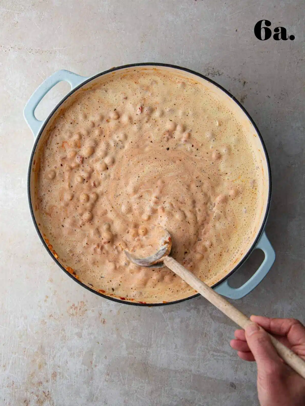Chickpeas cooking in a creamy sauce in a pan while stirred.