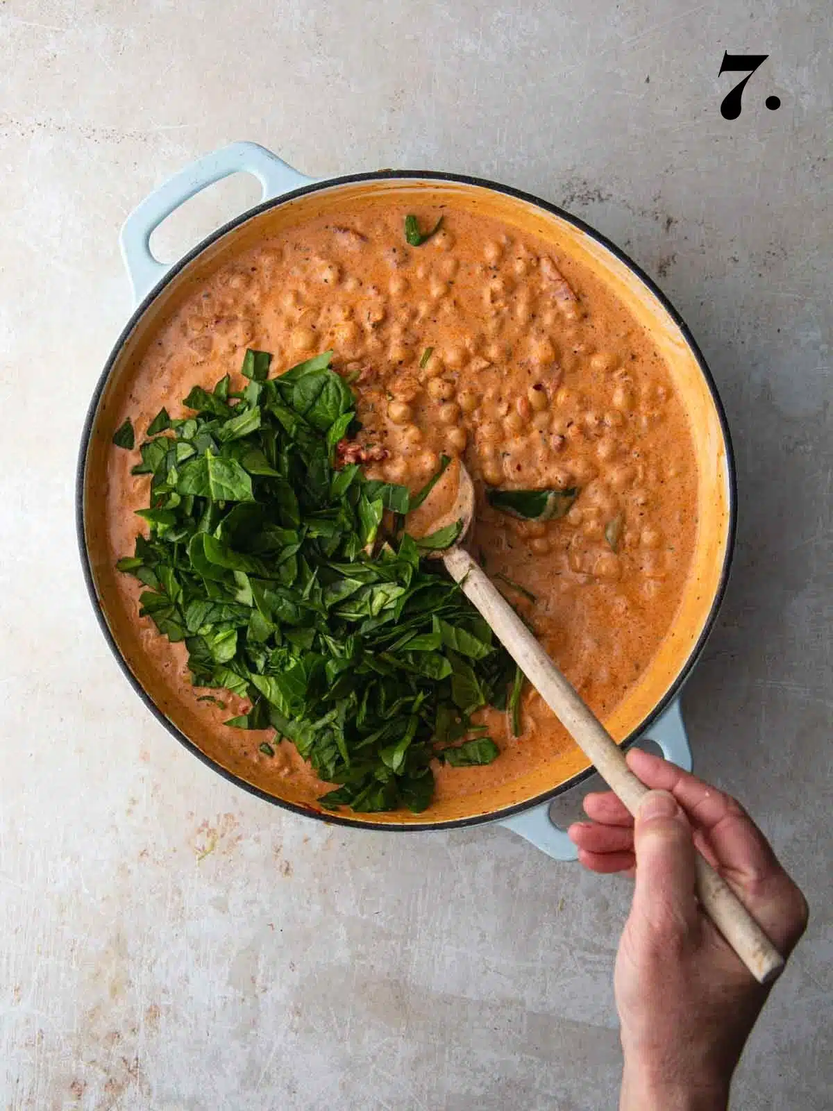 Creamy tomato chickpeas with spinach added to a large pan cooking.