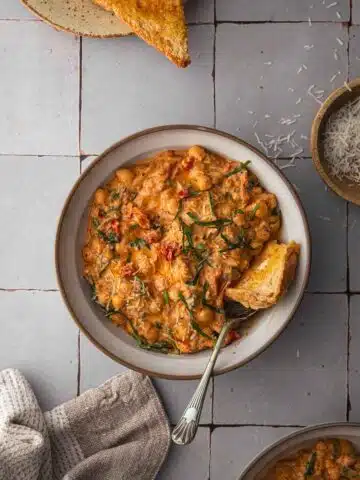 A bowl of Marry Chickpeas with toast and parmesan cheese on a tile tabletop.