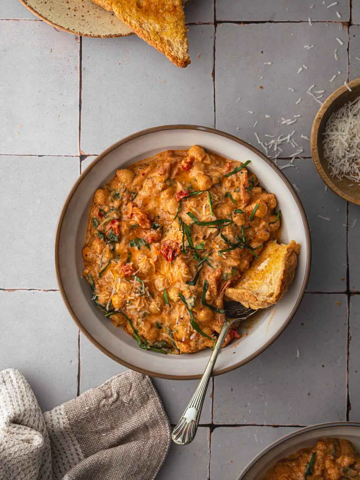 A bowl of Marry Chickpeas with toast and parmesan cheese on a tile tabletop.