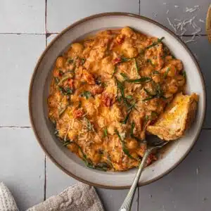 A bowl of creamy chickpeas with sun-dried tomatoes and fresh basil with toast.