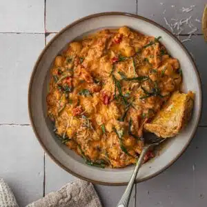 A bowl of Marry Chickpeas with toast and parmesan cheese on a tile tabletop.