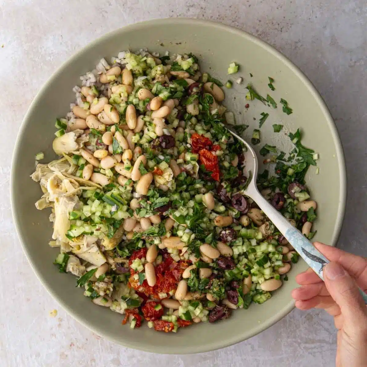 A bowl of white beans and tomato salad in a green bowl with a spoon.