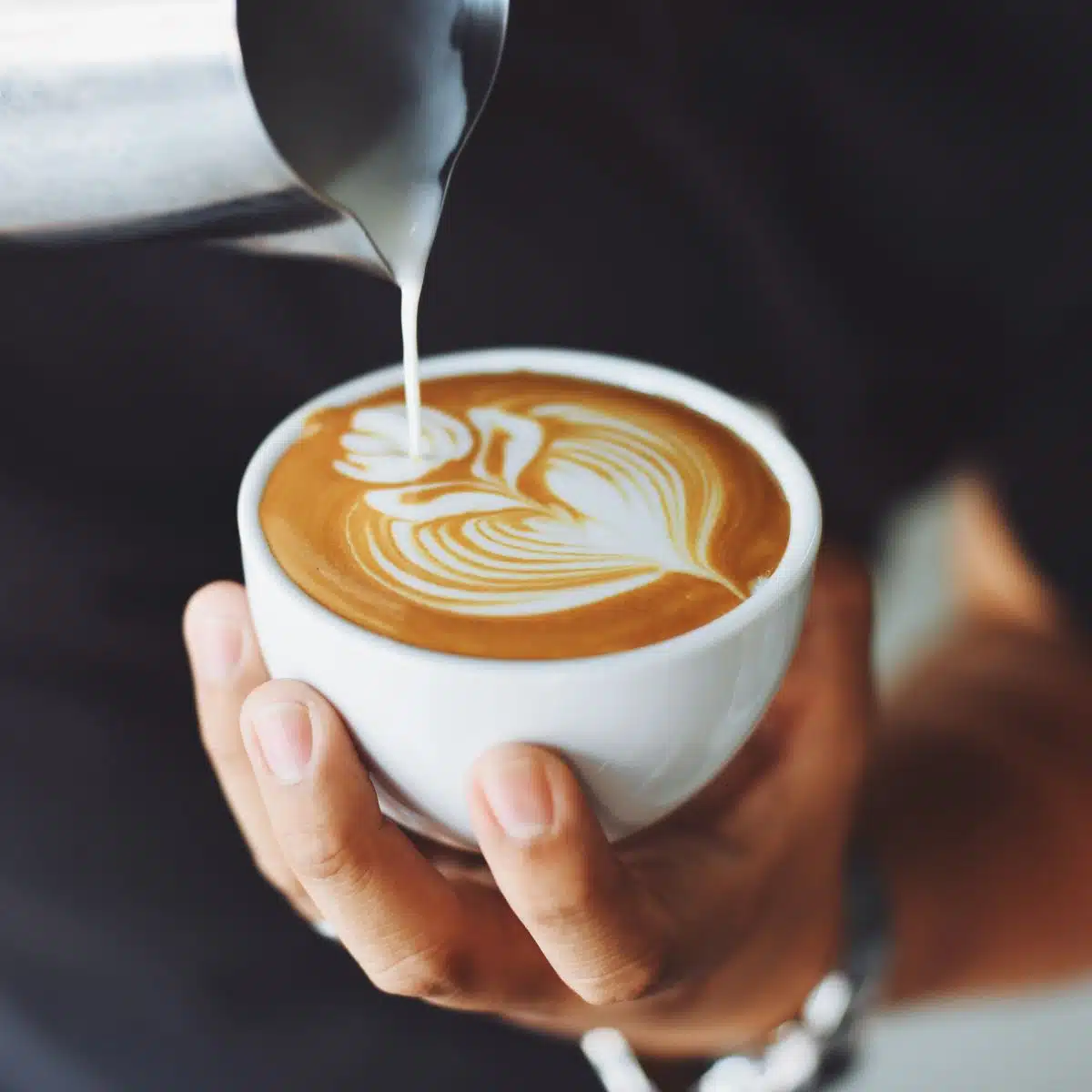 A barista pouring milk into a coffee cup.